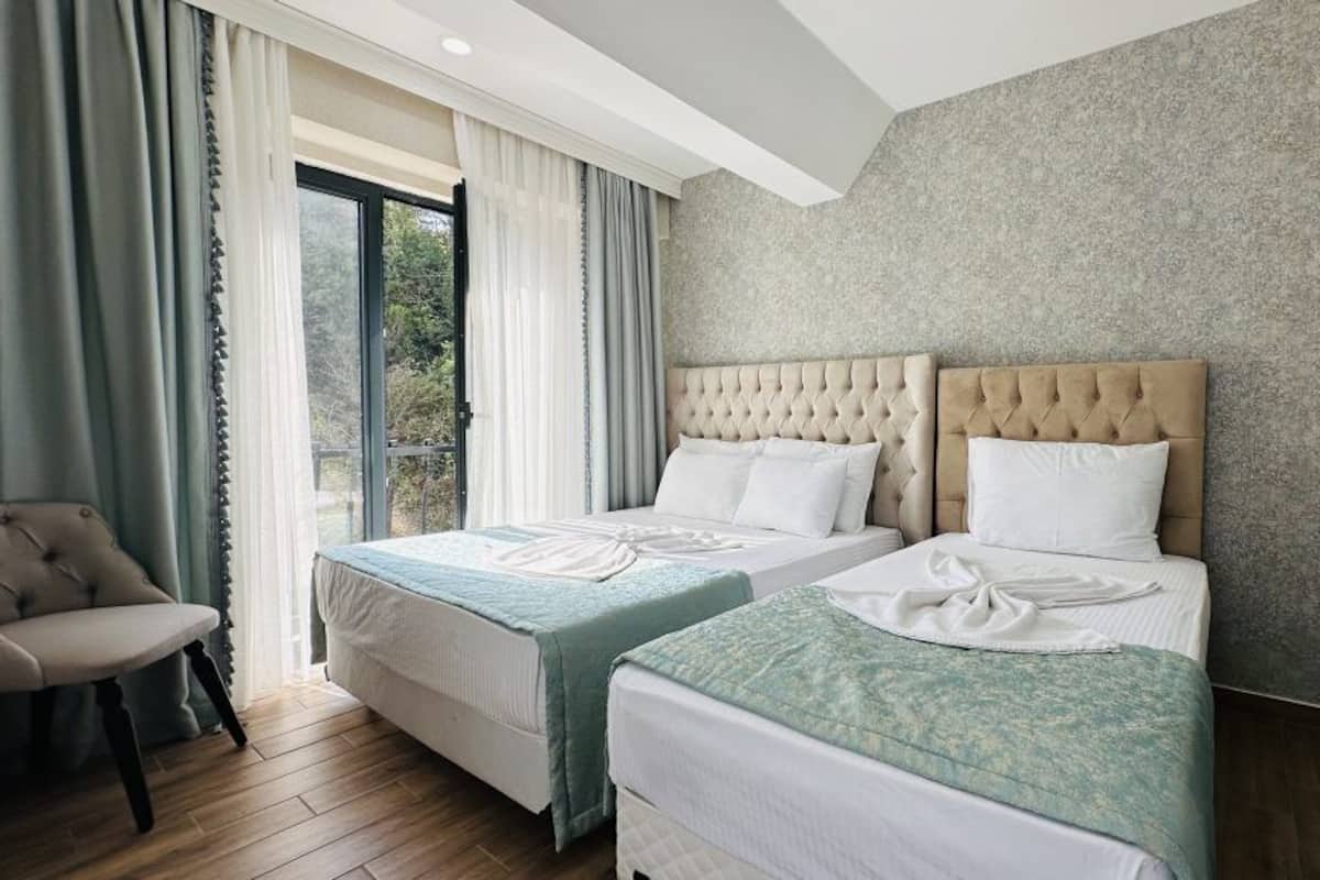 A hotel room with two beds, a sofa, and a large window with curtains.