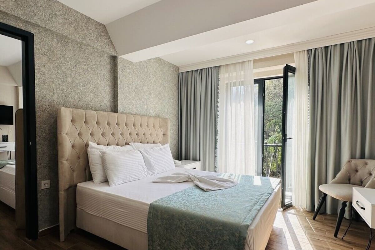 A modern hotel room with a large bed, a sitting area, and a balcony.