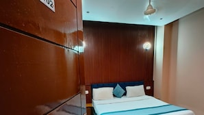 Een hotelkamer met een grote kledingkast, een bed met een blauw-witte dekbedovertrek, en een plafondventilator.