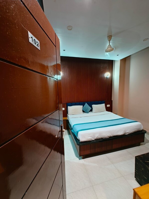 A hotel room with a large wardrobe, a bed with a blue and white bedspread, and a ceiling fan. - The Royal Hotel (Bareilly)