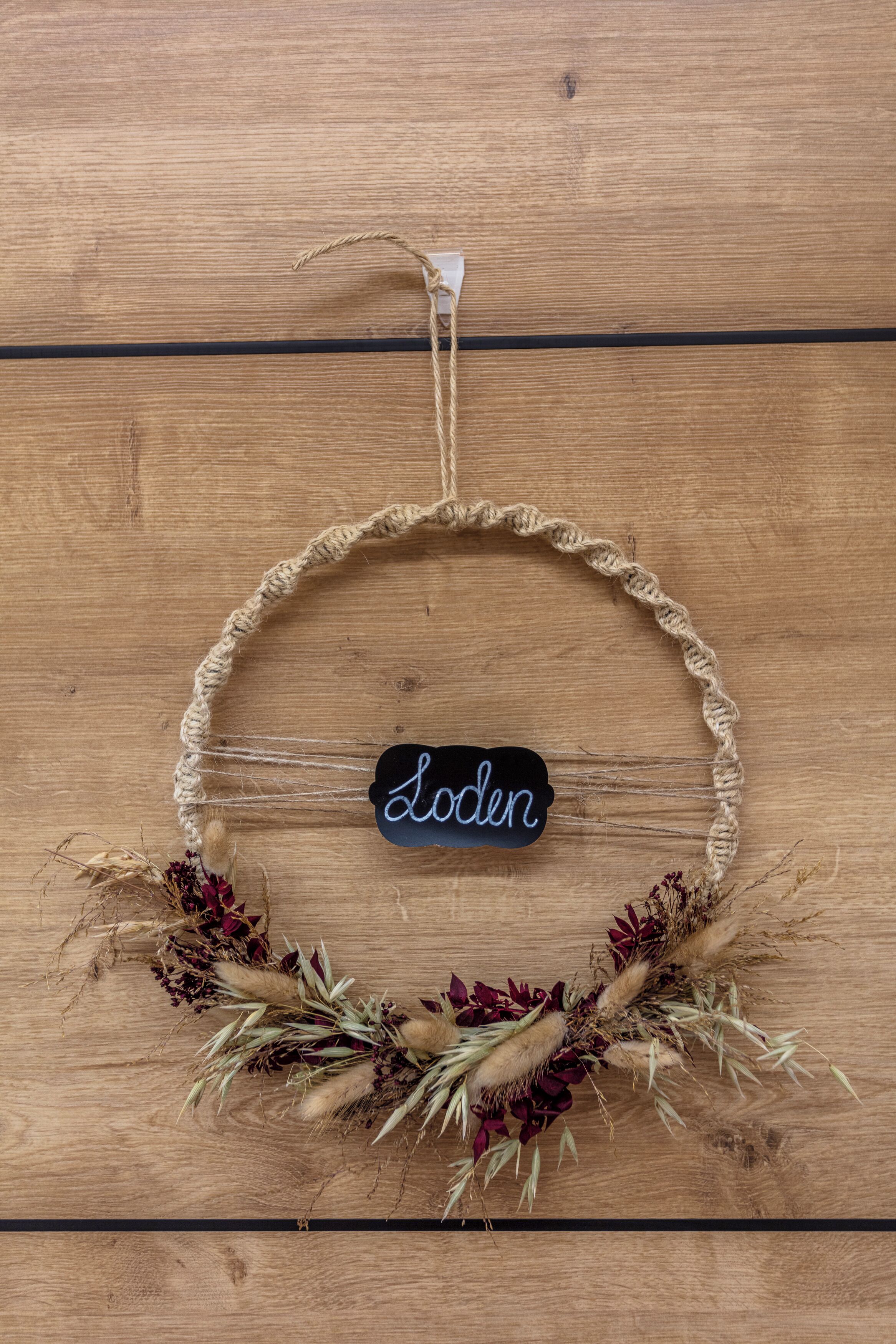 A macrame wall hanging with a name tag on a wooden background.