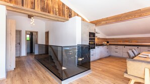 A modern kitchen with wooden accents, a glass staircase, and a dining area with a wooden table. - Obermühlhof (Saalfelden am Steinernen Meer)