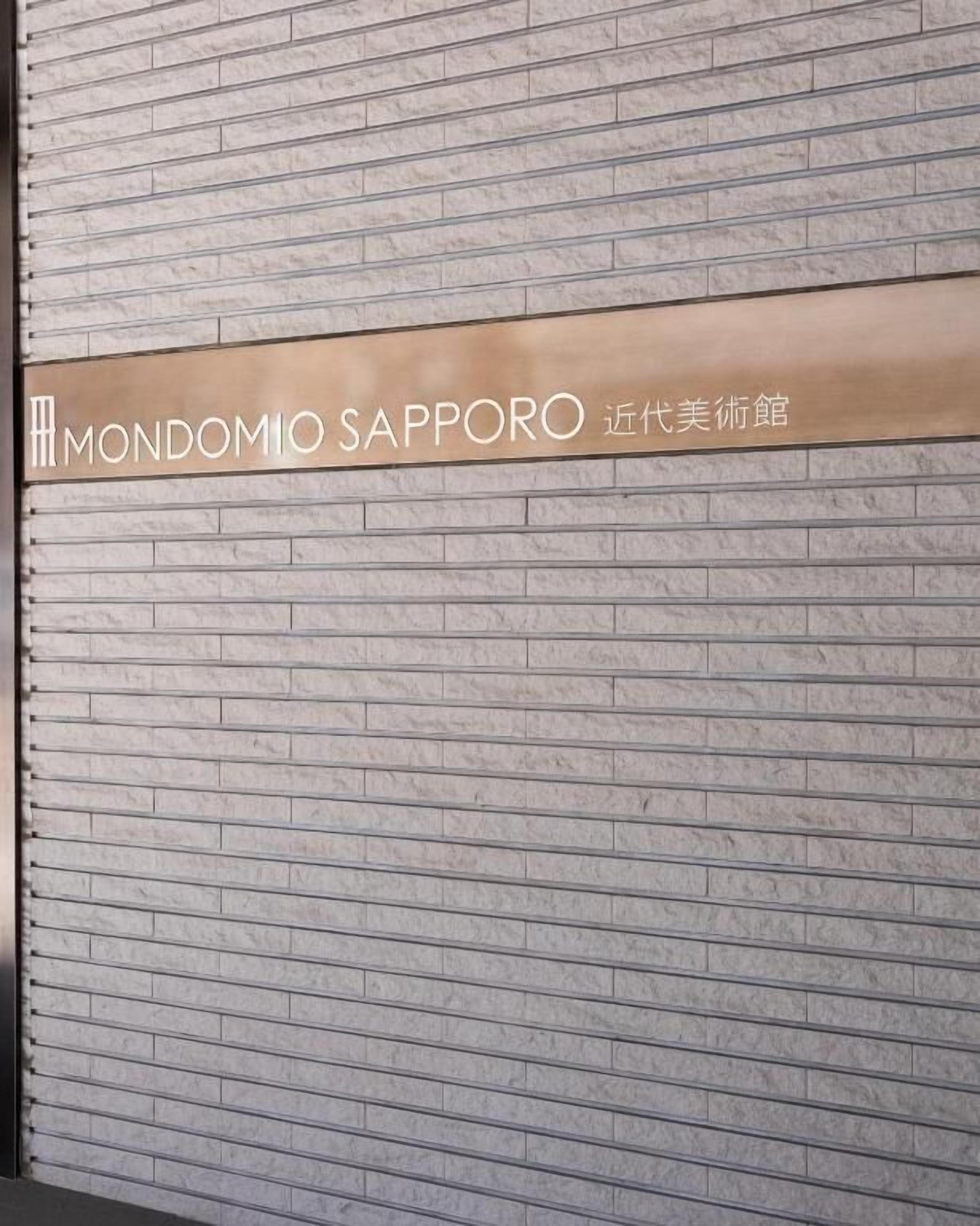 Um sinal com o texto 'MONDOMIO SAPPORO' numa parede de tijolos.