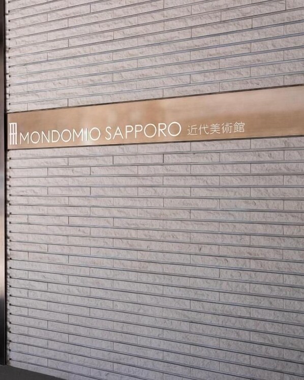 A sign with the text 'MONDOMIO SAPPORO' on a brick wall.