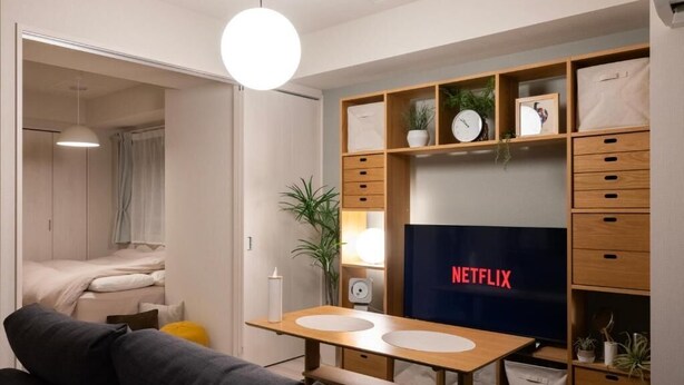 A modern living room with a TV displaying 'NETFLIX', a wooden TV stand, a sofa, a dining table, and a wardrobe. - Mondomio Sapporo 510 (Sapporo)