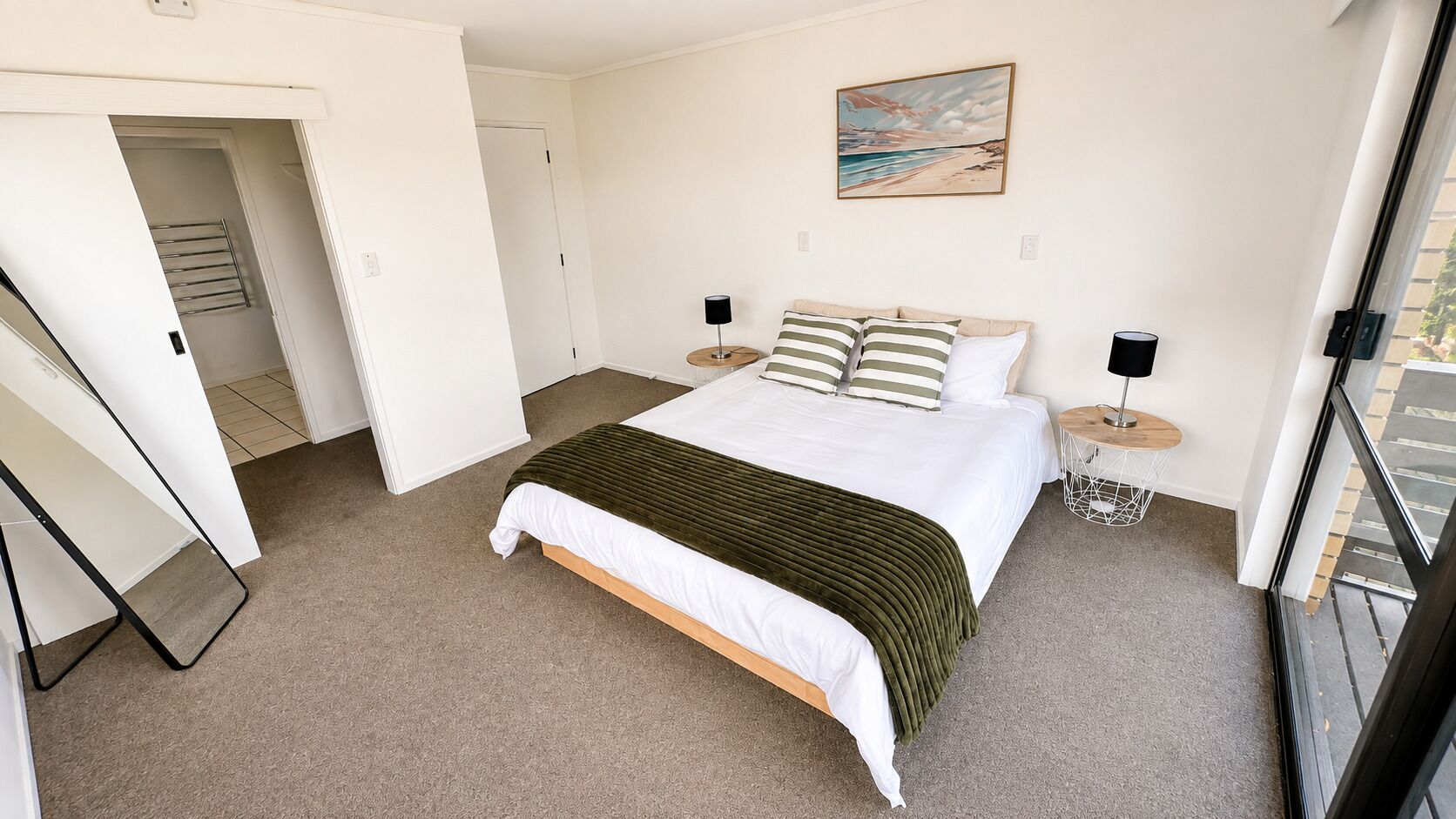 A bedroom with a bed, bedside tables, a painting, and a view through a window.