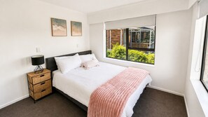 Une chambre à coucher avec un lit, une table de chevet avec une lampe, une fenêtre donnant sur un paysage verdoyant et deux tableaux accrochés au mur.