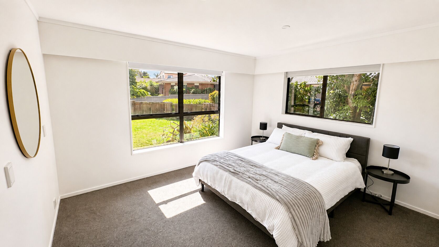 A bedroom with a bed, two bedside tables, a window, and a mirror.