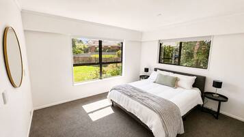 A bedroom with a bed, two bedside tables, a window, and a mirror.