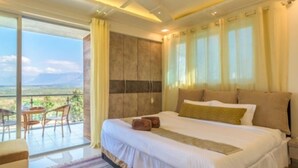 A hotel room with a large bed, a balcony with a table and chairs, and a view of the landscape. - Tranq Villa by Stay Serene Luxury (Murbad)
