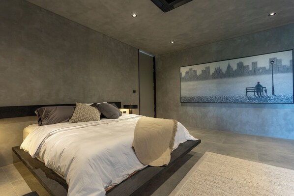 Un dormitorio moderno con una cama grande, un cuadro de un paisaje urbano en la pared y un diseño minimalista.