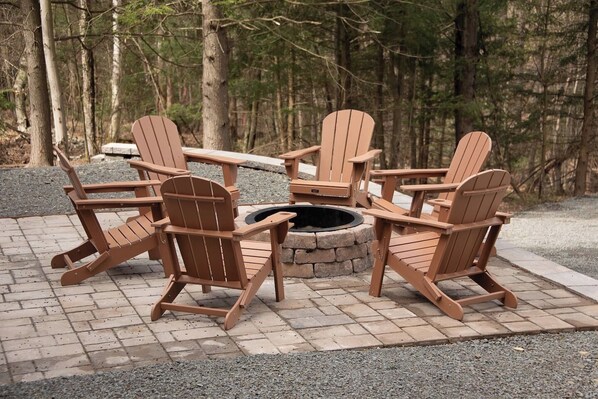A circular fire pit surrounded by four Adirondack chairs.