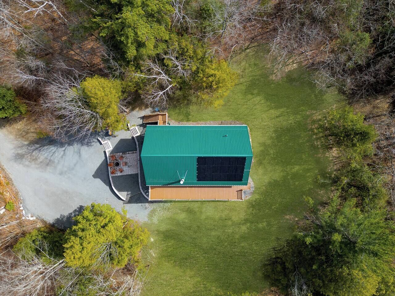 An aerial view of a single-story building with a green roof, surrounded by a well-maintained lawn and dense trees.