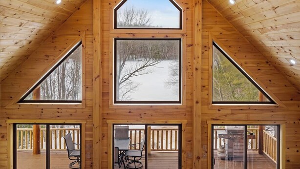 Una cabaña de troncos con techo inclinado, ventanas amplias y un candelabro.