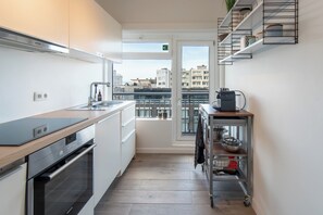 Una cocina estrecha con horno empotrado, un lavabo y una ventana con vistas a un paisaje urbano.
