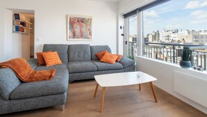 Un soggiorno moderno con un divano componibile grigio, un tavolino bianco e una grande finestra vista città.