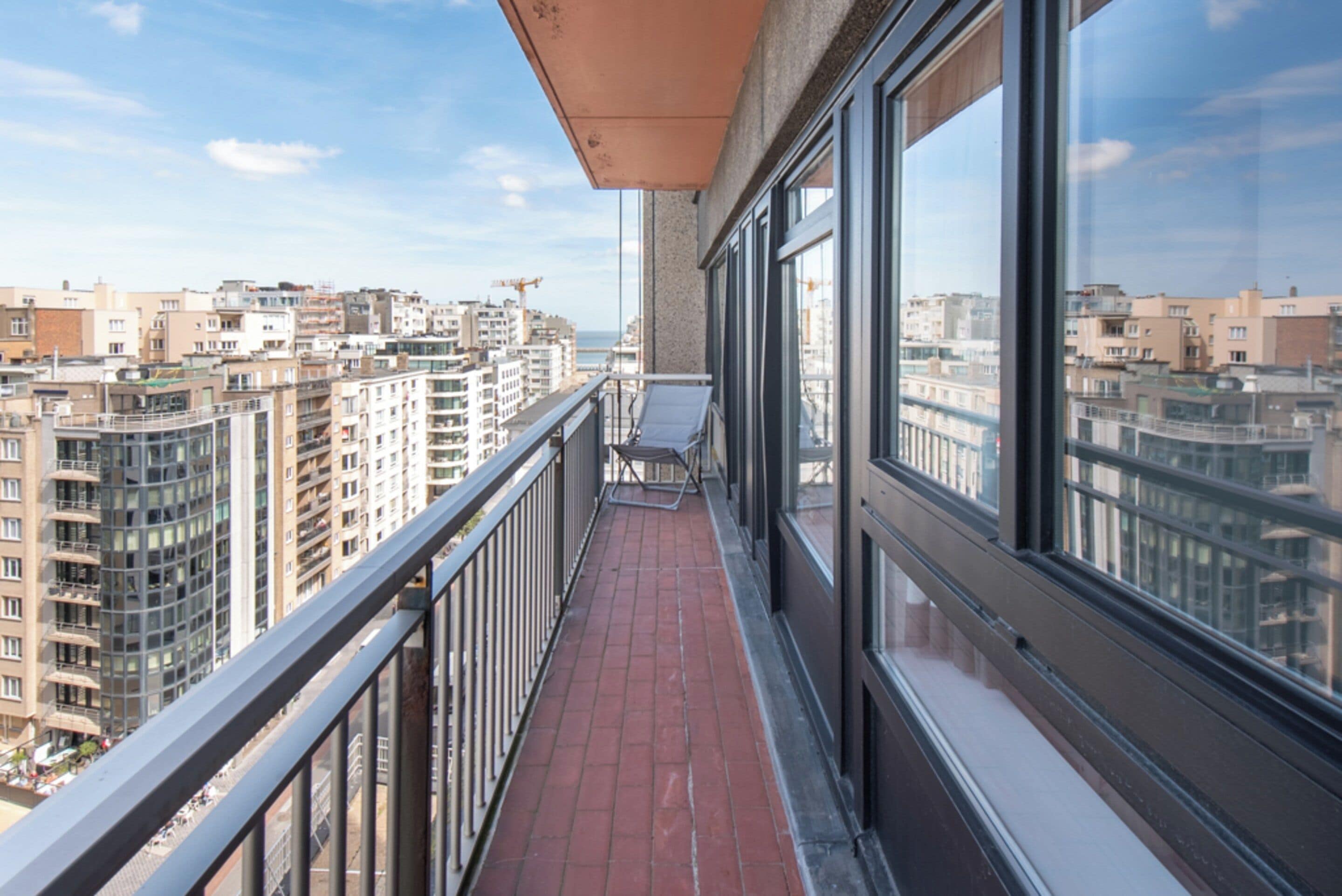 A balcony with a view of high-rise buildings, a metal railing, and a clear sky.
