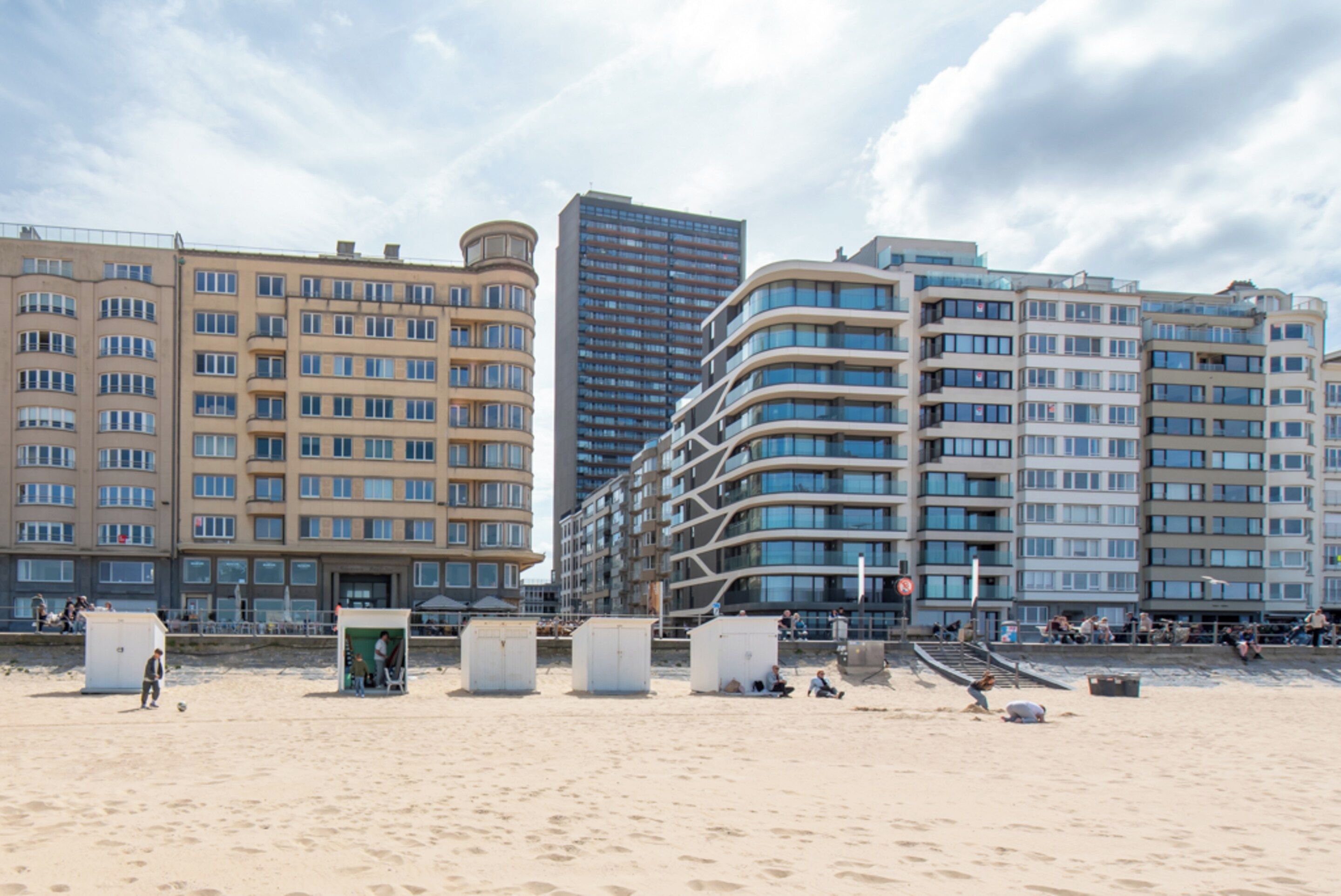 A beachfront hotel with multiple floors, a curved facade, and a sandy beach in the foreground.