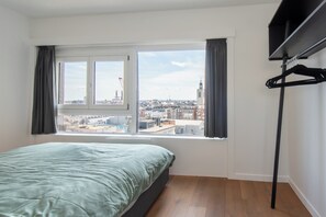 Un dormitorio con una cama, una ventana con cortinas y vistas a un paisaje urbano.