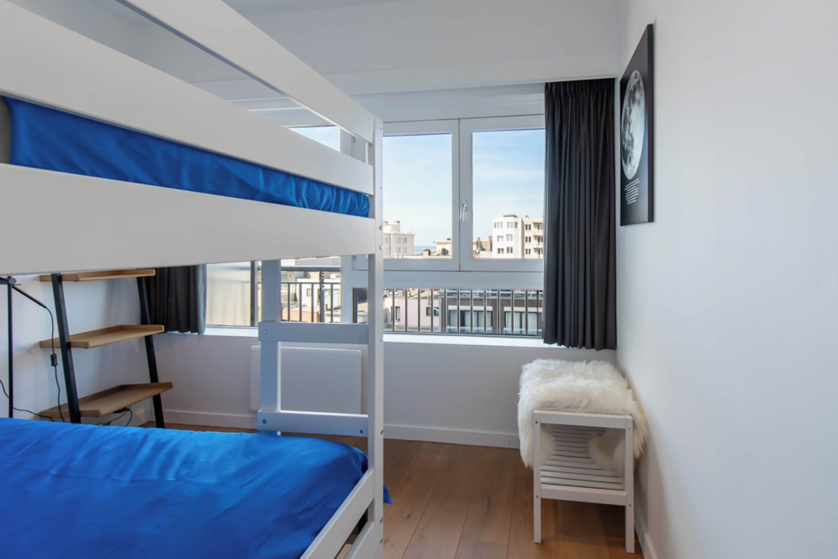 A bunk bed room with a city view, a white radiator, and a small white chair.