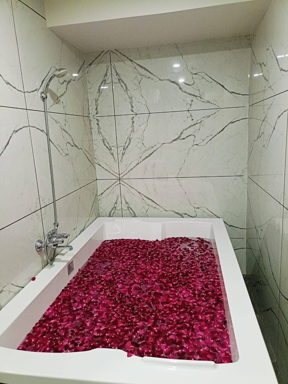Una bañera llena de pétalos de rosa, un cabezal de ducha y paredes con diseño de mármol.