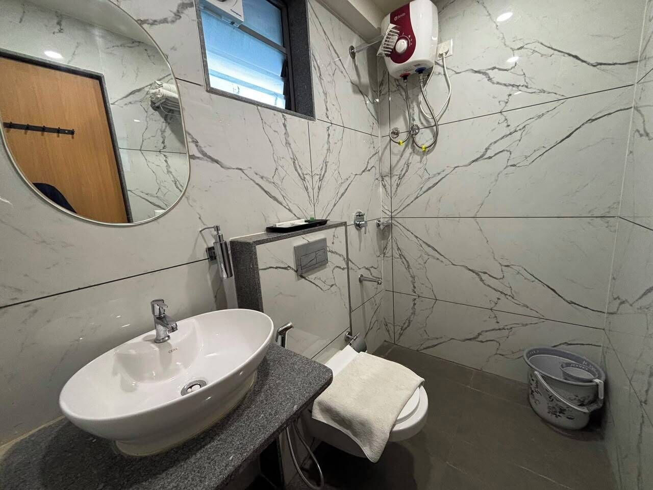 Un baño con lavamanos blanco, toallero, ducha y pared de mármol.