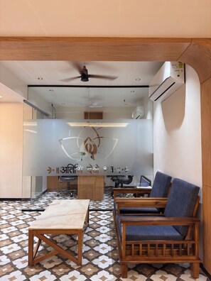 Una habitación moderna con una mesa de madera, dos sillas azules, un ventilador de techo y un equipo de aire acondicionado.