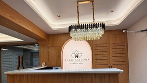 A reception desk with a chandelier, wooden paneling, and a logo for Royal Galleria. - Hotel Royal Galleria (Vadodara)
