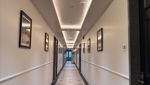 A long, narrow hotel hallway with a tiled floor, framed pictures on the walls, and recessed lighting. - Hotel Royal Galleria (Vadodara)