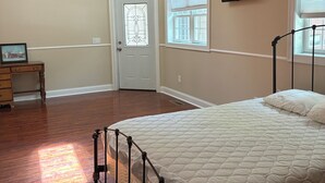 Un dormitorio con cama, cómoda, puerta con panel de vidrio, ventana con persianas y televisor en la pared.