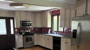 Una cocina con suelo de madera, armarios blancos, electrodomésticos de acero inoxidable y una ventana con vistas.