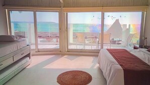 A bedroom with a bed, a dresser, and a view of the sea through large sliding doors.