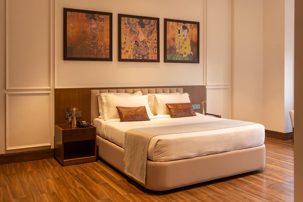 A spacious bedroom with a large bed, a nightstand, and three framed artworks on the wall.