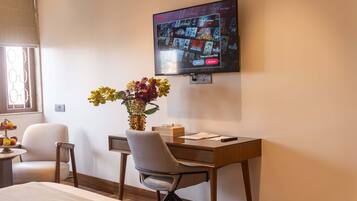 A hotel room with a bed, a desk with a chair, a television mounted on the wall, and a vase with flowers on the desk.