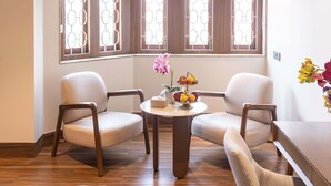 A corner room with two white chairs, a small round table with a fruit bowl and a potted plant, and a window with a geometric pattern. - Park Suites (Kolkata)