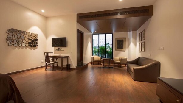 A spacious living room with a wooden floor, a flat-screen TV, a dining area with chairs, and a sofa. - Park Suites (Kolkata)