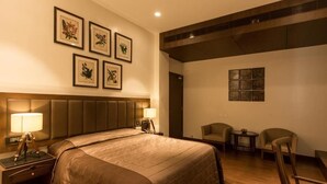A hotel room with a large bed, two bedside lamps, a headboard, a small table with a chair, and framed artwork on the walls. - Park Suites (Kolkata)