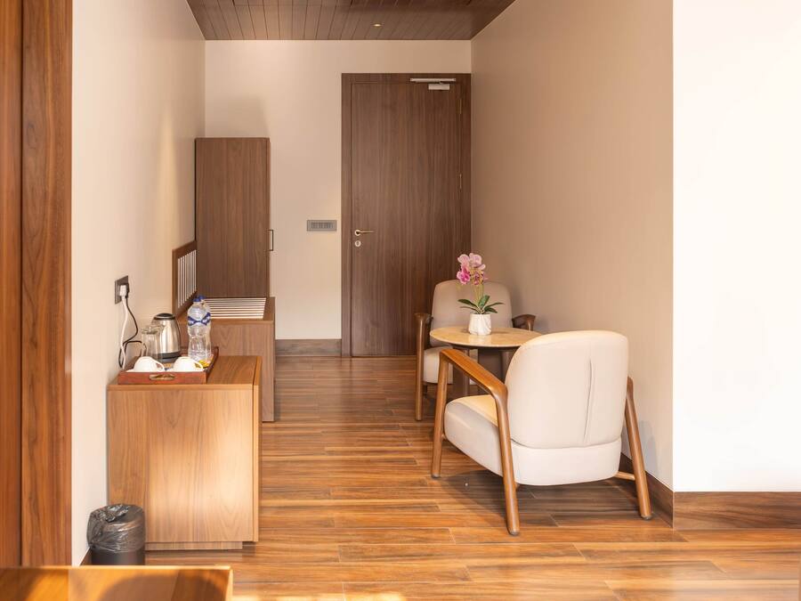 Ein modernes Hotelzimmer mit Holzboden, einem Holztisch mit Pflanze, einem weißen Sofa und einer Tür im Hintergrund.