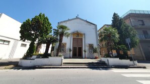 Eine weiße Kirche mit einem zentralen Eingang, gesäumt von Palmen und Kübelpflanzen.