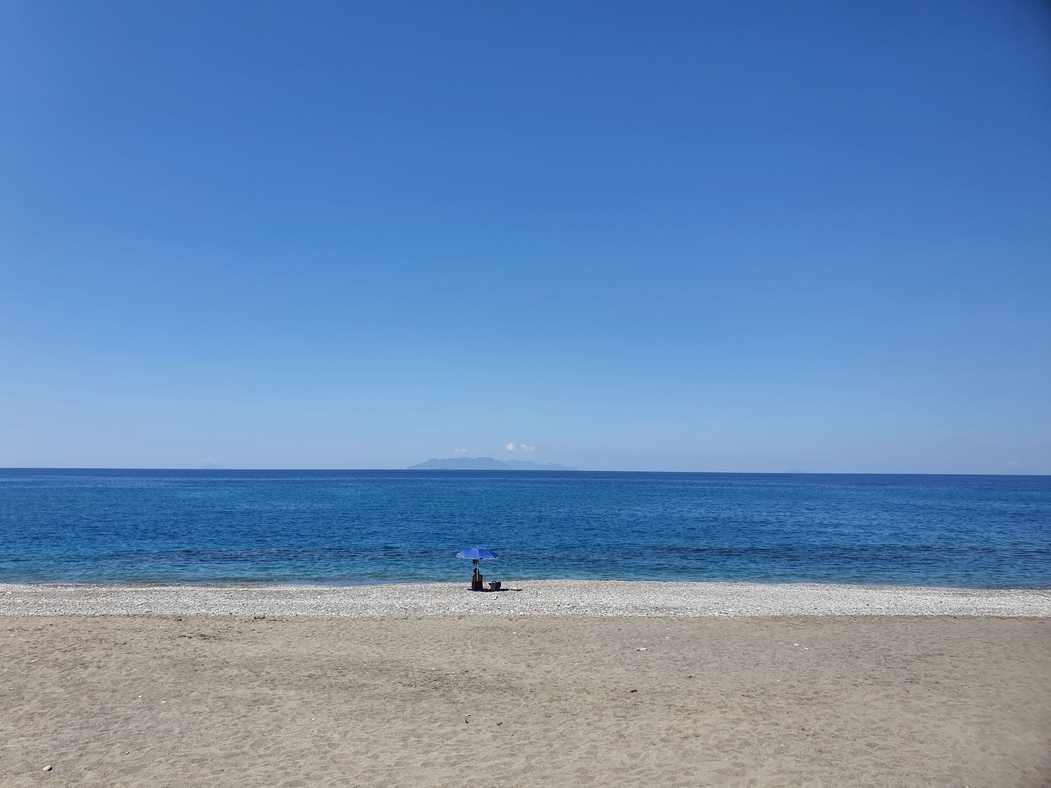 A beach with a clear view of the ocean and a distant mountain.