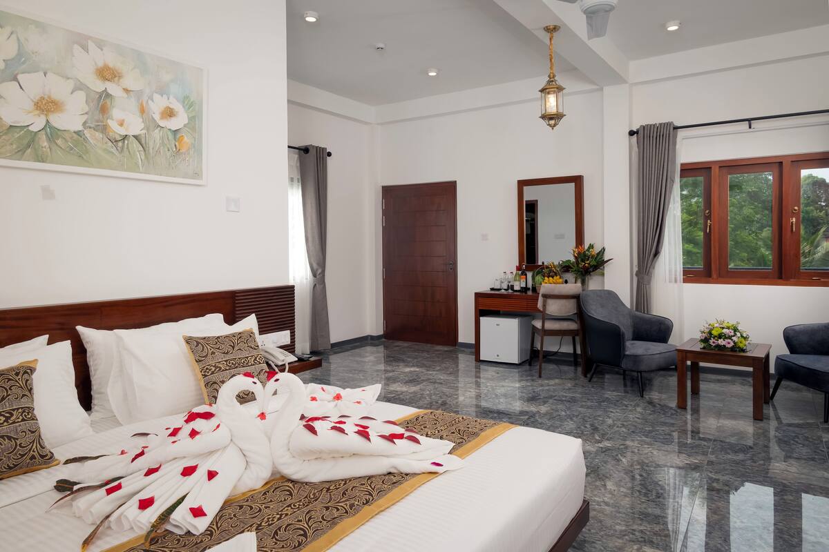A hotel room with a neatly made bed, a desk, a chair, and a large window with curtains.