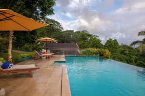 An infinity pool with lounge chairs and umbrellas, surrounded by lush greenery and a clear sky. - Mirage Kandyan Heights (Kandy)