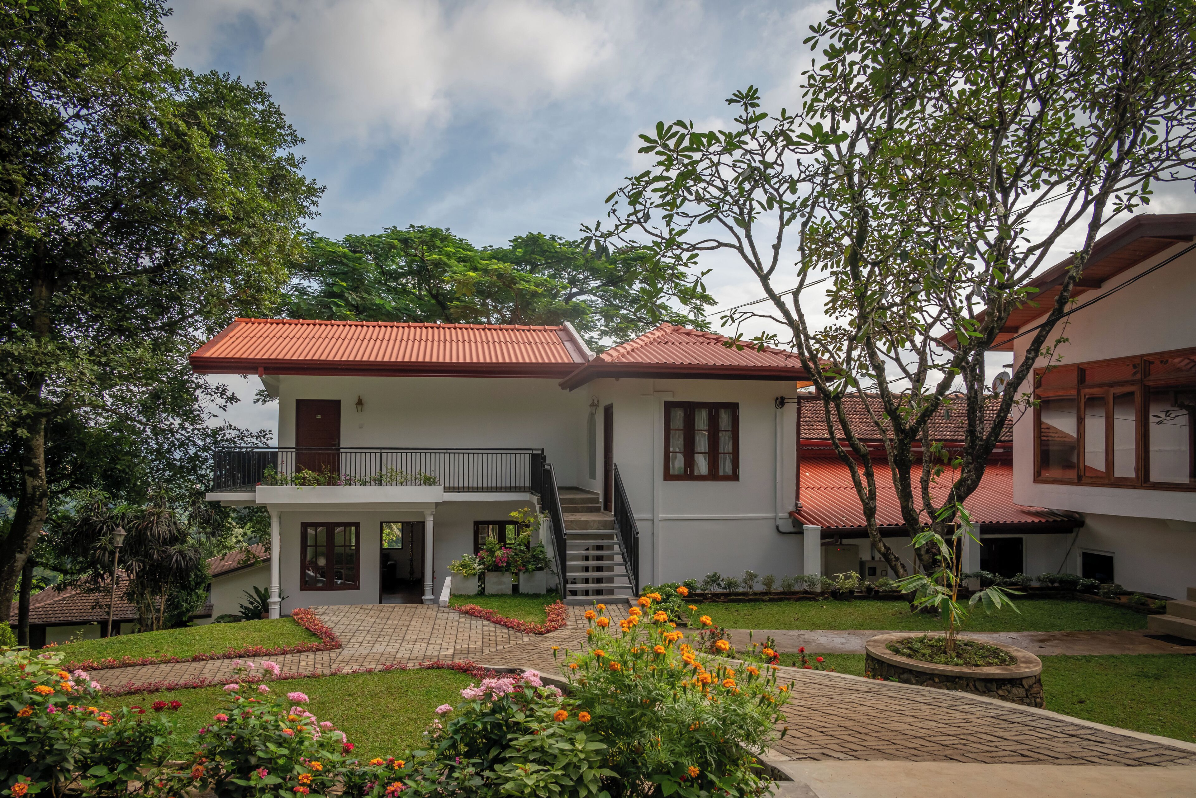 Uma casa de dois andares com telhado vermelho, varanda e um jardim florido.