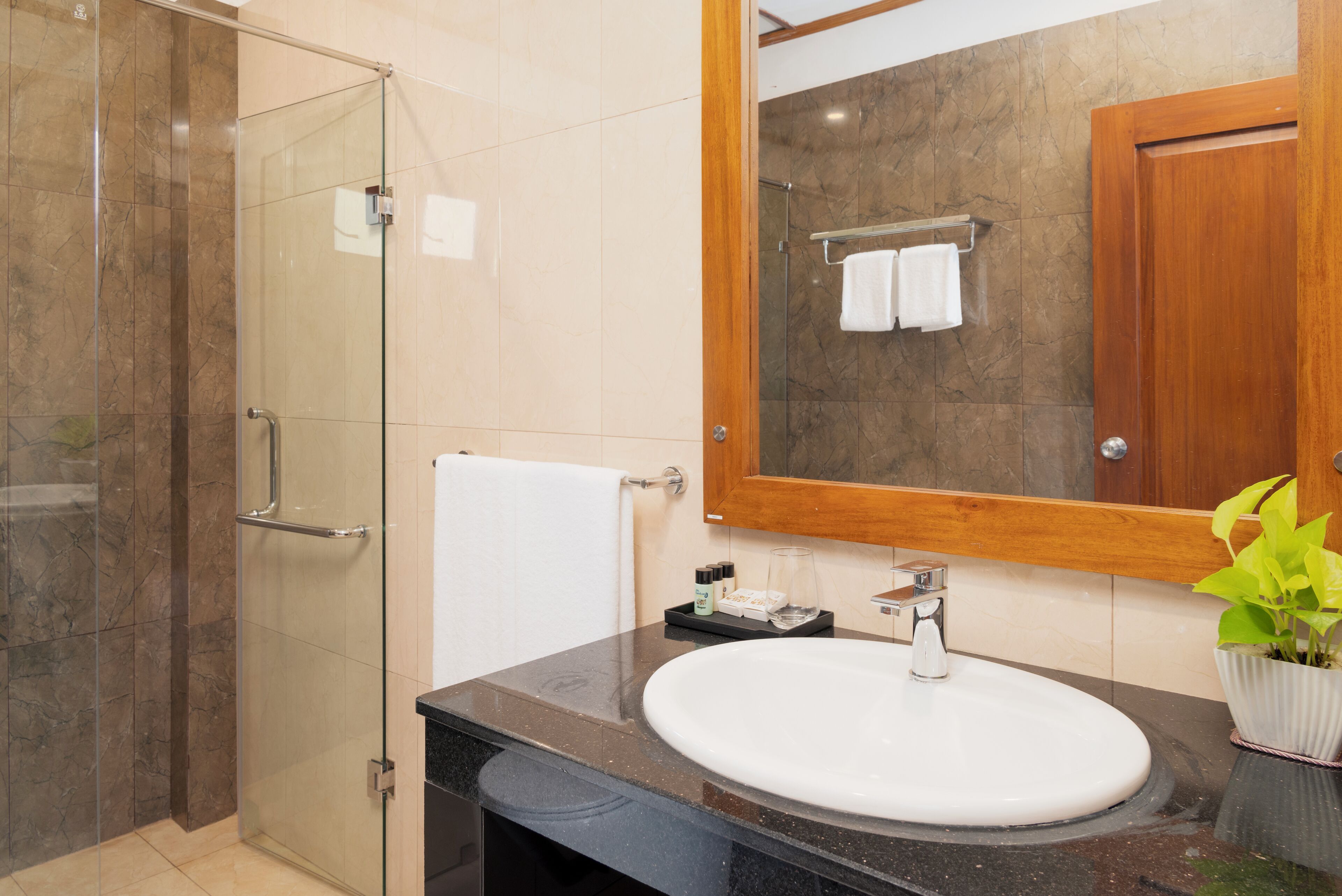 A modern bathroom with a glass-enclosed shower, a white sink, and a wooden-framed mirror.
