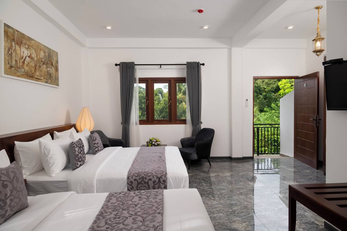 A hotel room with two beds, a chair, a lamp, a painting, a window with curtains, and a balcony with a view of greenery.