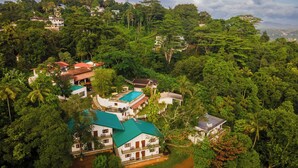 An aerial view of a resort with multiple buildings surrounded by dense greenery, including palm trees and other tropical vegetation. - Mirage Kandyan Heights (Kandy)