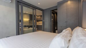 A modern hotel room with a large bed, a walk-in closet, and a bathroom visible through an open door. - FullyLoadedBestFacilitiesNicestAptc141 (Kamala)