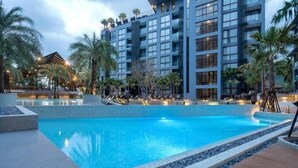 A modern hotel with a large swimming pool, palm trees, and a well-lit outdoor area. - FullyLoadedBestFacilitiesNicestAptc141 (Kamala)