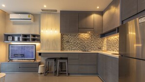 A modern kitchen with grey cabinets, a stainless steel refrigerator, a tiled backsplash, and a built-in TV. - FullyLoadedBestFacilitiesNicestAptc141 (Kamala)