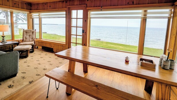 A wooden cabin with a large dining table, a ceiling fan, and a view of the lake. - Lake Huron Cottage with Private Beach Access, walking distance to Port Sanilac (Port Sanilac)